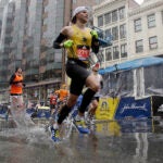 Timothy McFadden, of Boston, splashes through a puddle after finishing the 122nd Boston Marathon in the rain.