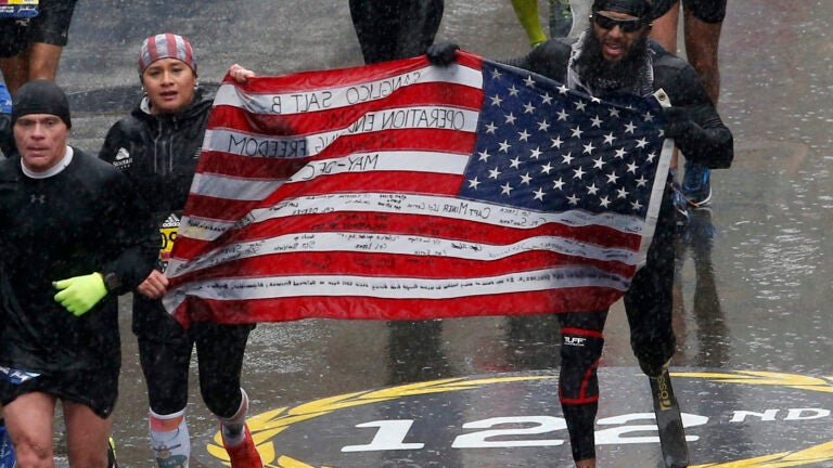 Runners carry a flag towards the finish line of the 122nd Boston Marathon.