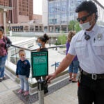 A security guard adjusts a "Social Distance" sign