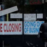 A woman looks at signs at a store closed due to COVID-19.