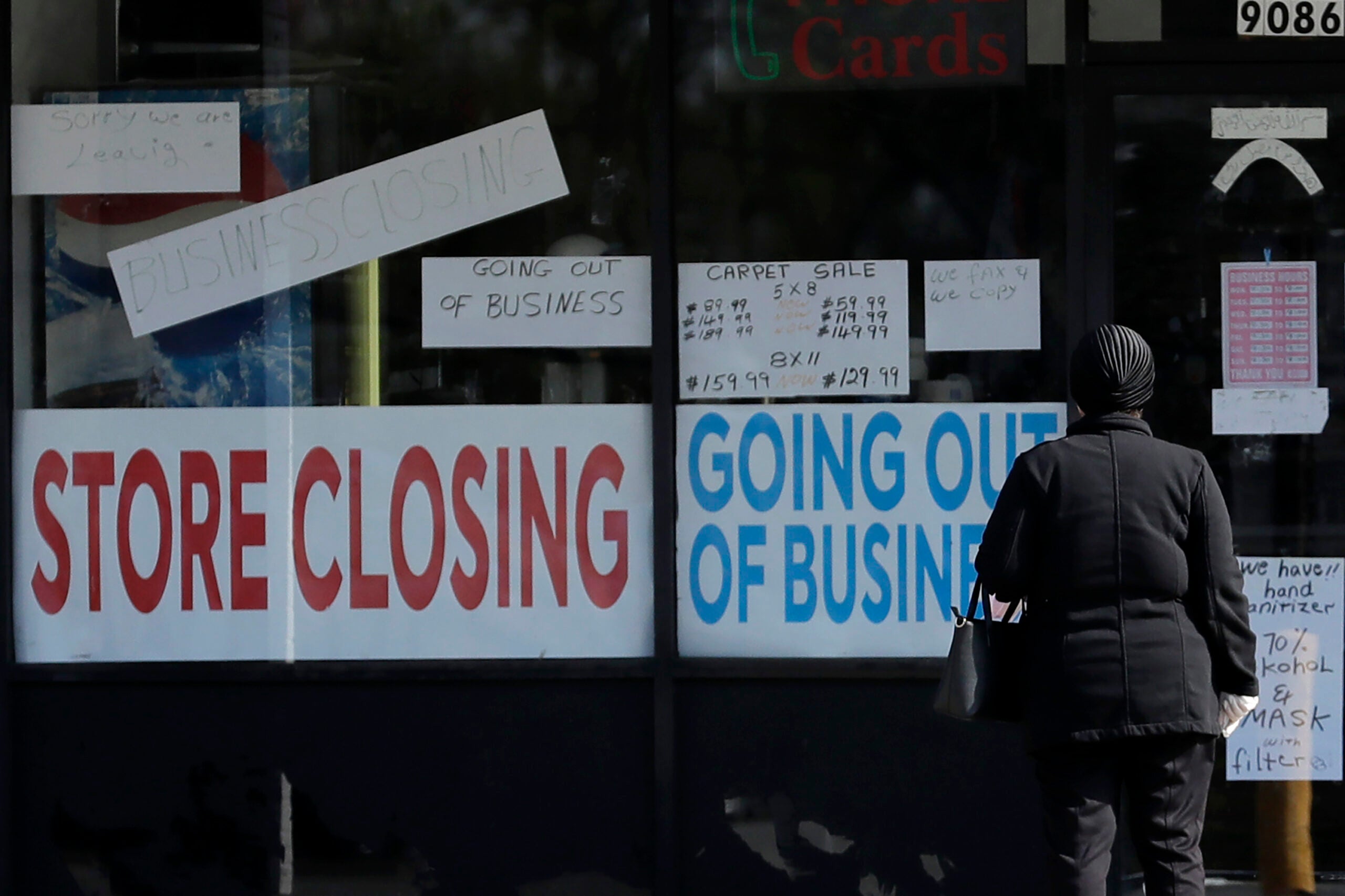 A woman looks at signs at a store closed due to COVID-19.