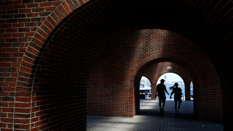 People are silhouetted as they walk through an archway at Long Wharf.