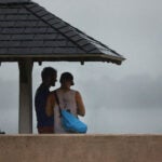 Two people take shelter from rain on a South Boston beach.