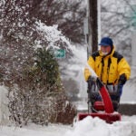 A man uses a snowblower to clear the sidewalk.