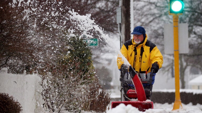 A man uses a snowblower to clear the sidewalk.