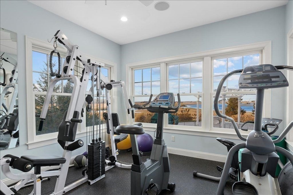Gym equipment is set up facing out a panel of three windows. The windows offer a view of the marsh and river.