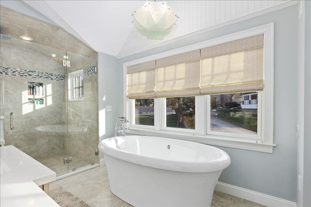 A white soaking tub sits under a panel of three windows. The standalone shower is visible in the background.