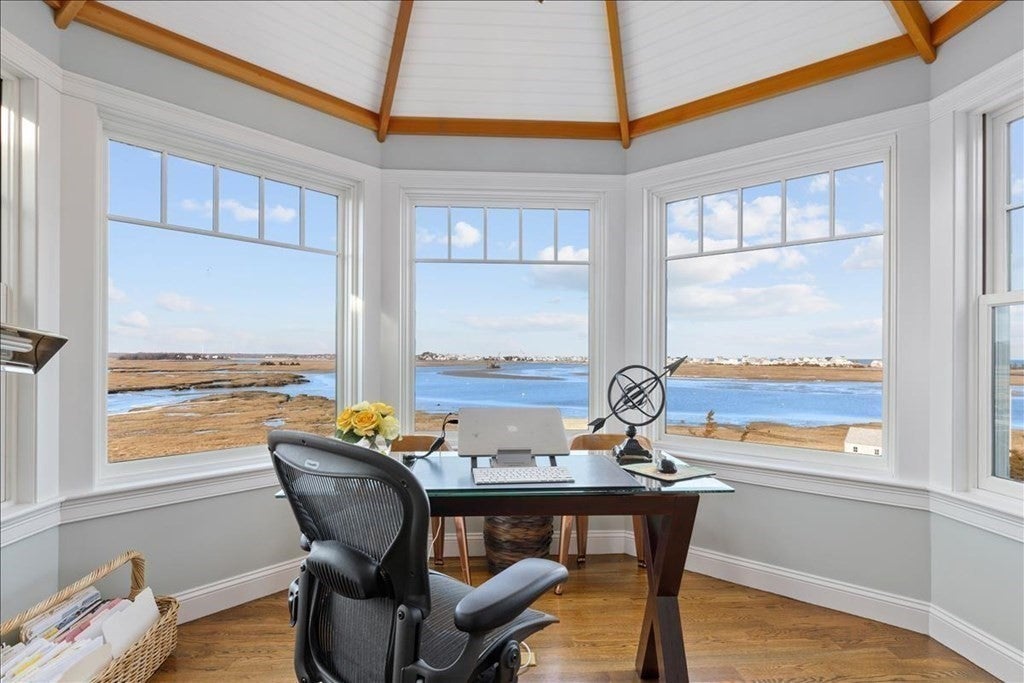 An office chair sits are a desk in a small room surrounded by windows. The marsh and river are visible from the windows.