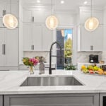 A kitchen island with a sink. Three round lights hang above the island. Recessed lighting and raised-panel cabinetry are visible in the background.