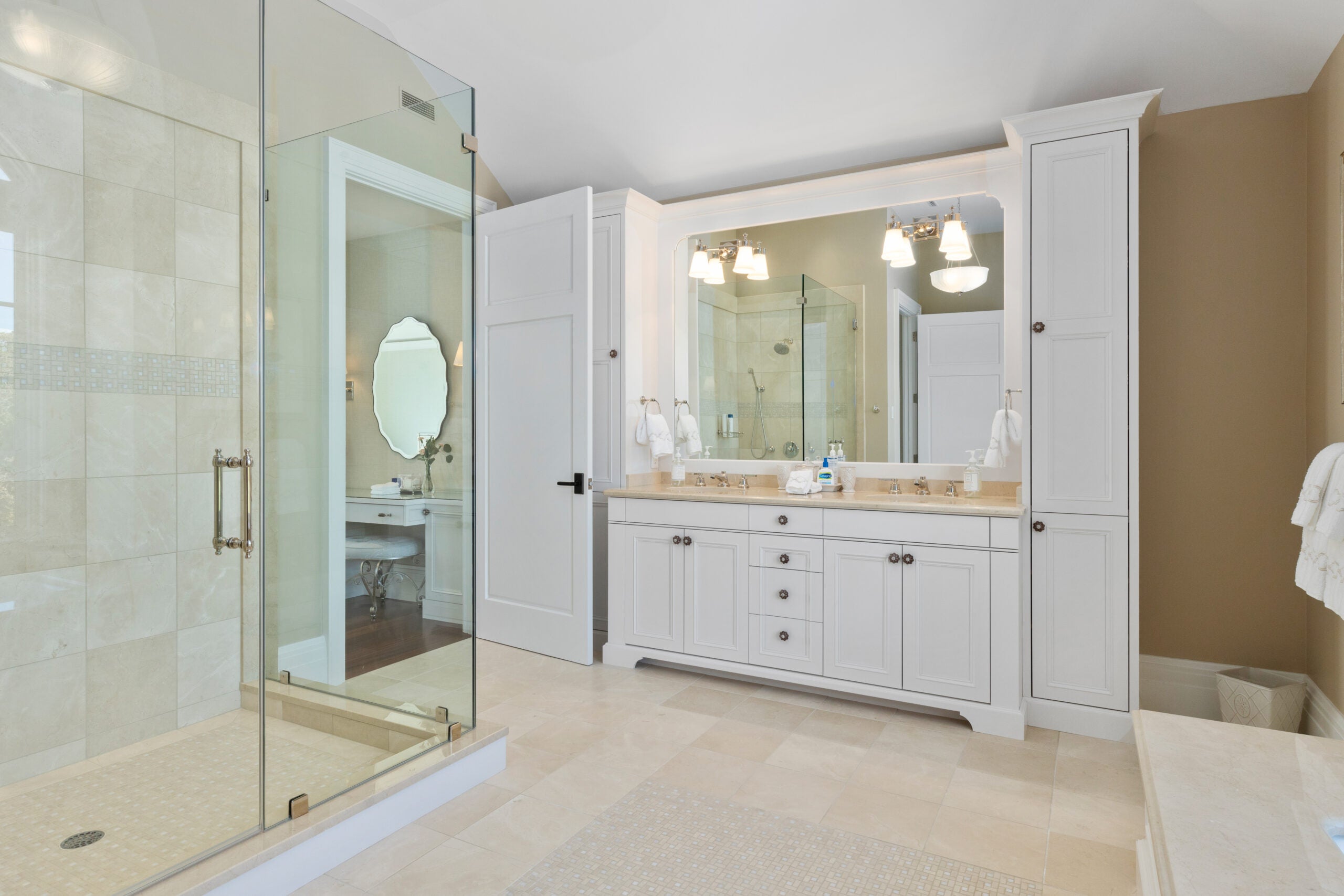 A bath with beige walls, white cabinetry, a dual vanity, and a curbed, frameless-glass shower. The counters are beige, as is the flooring tile.