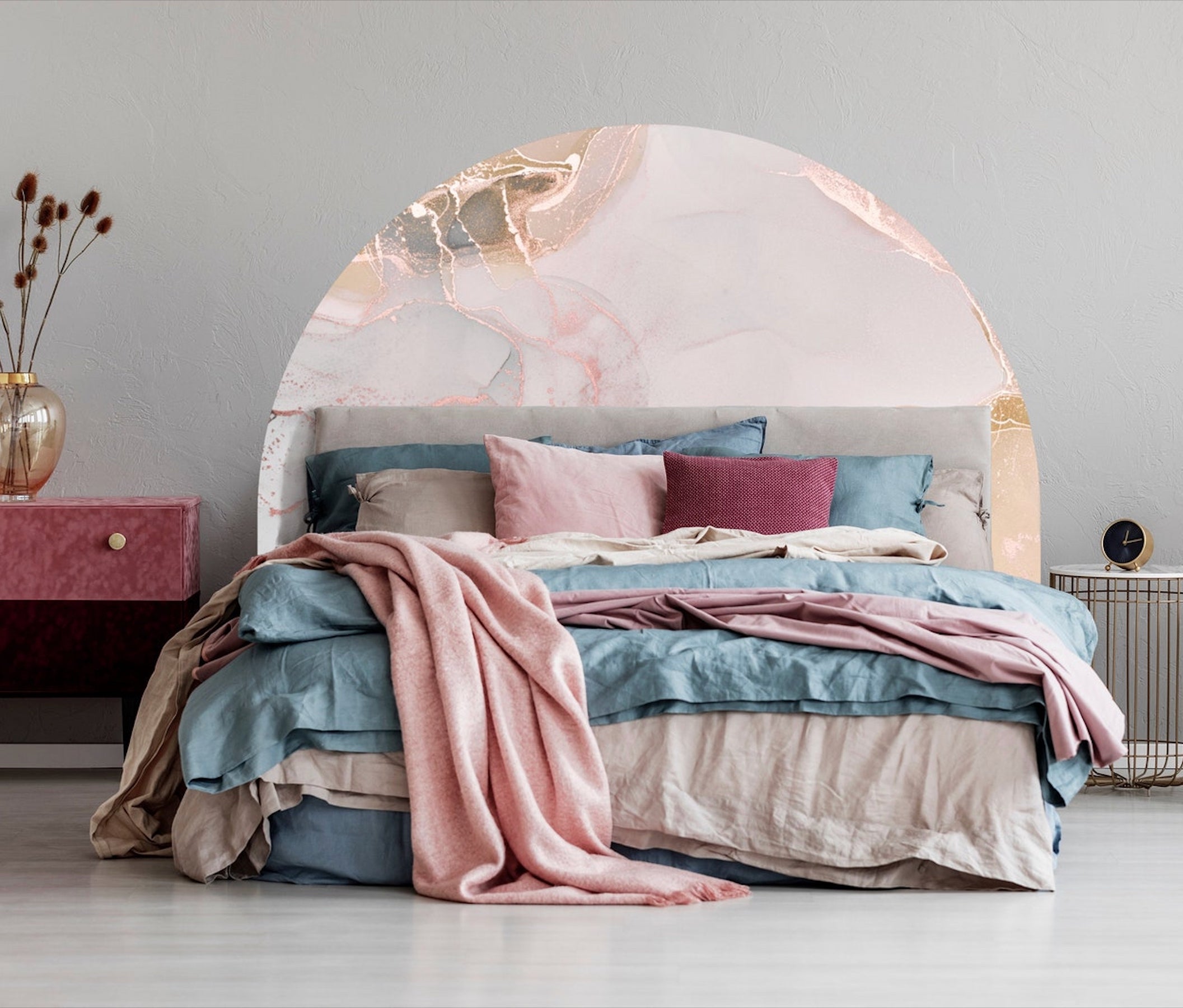 A decale of pinkish marble in an arch serves as a headboard for a bed with blue and pink bedding and blue, gray, red, and pink throw pillows.