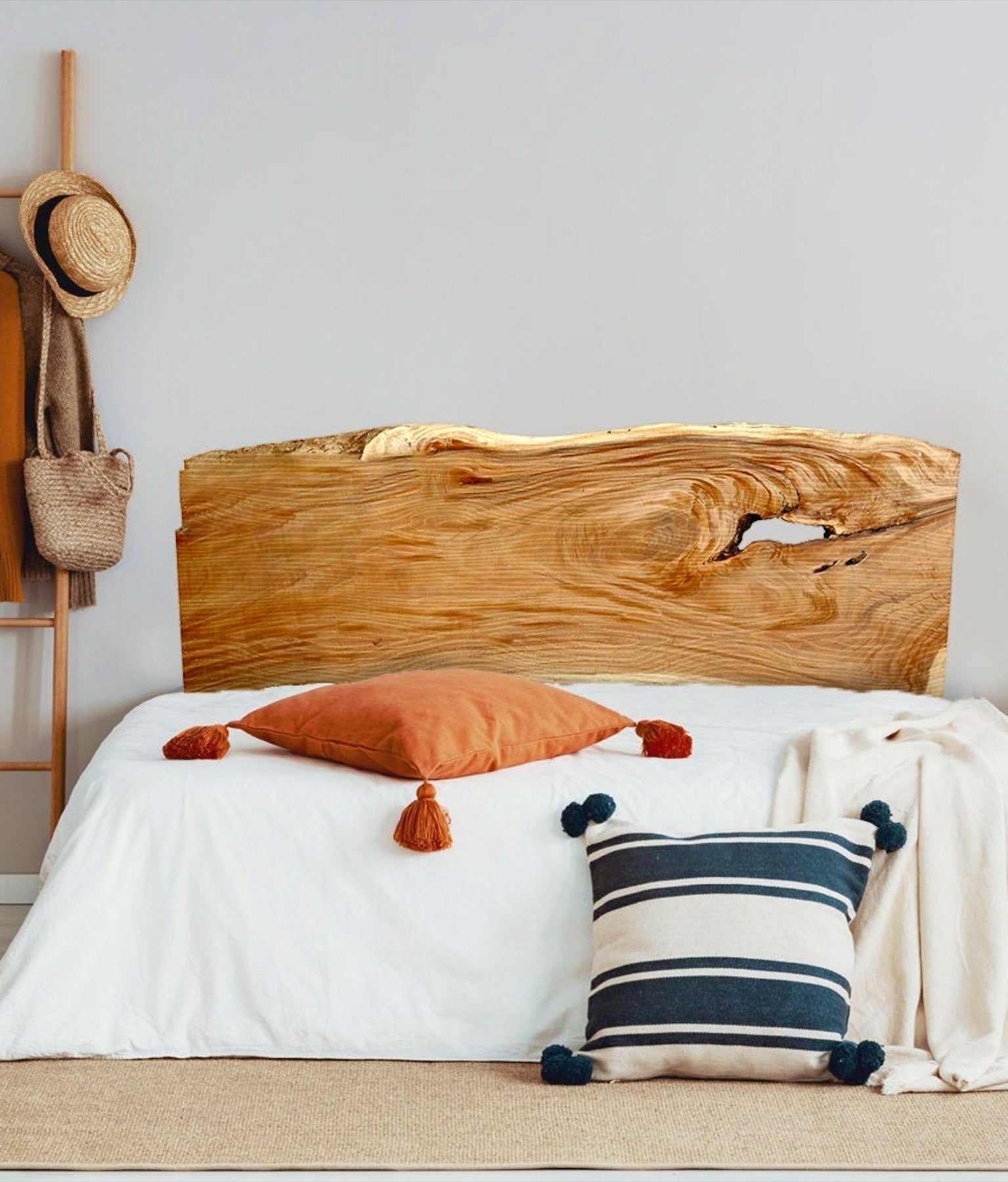 A decal that looks like live wood serves as a headline for a bed with white bedding and a blue-and-white striped and an rust-colored pillow with fringe. There is a hat stand in the background.