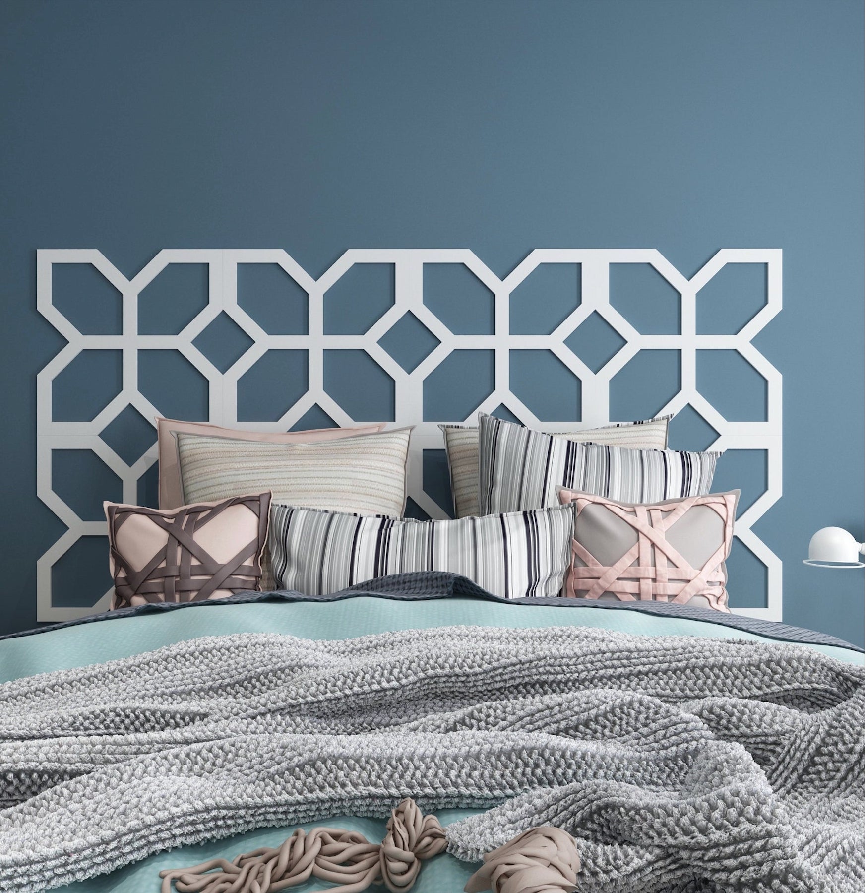 A white geometric decal in a trellis-like design serves as a headboard for a bed with gray and pink textured pillows and gray and aqua, very soft bedding.