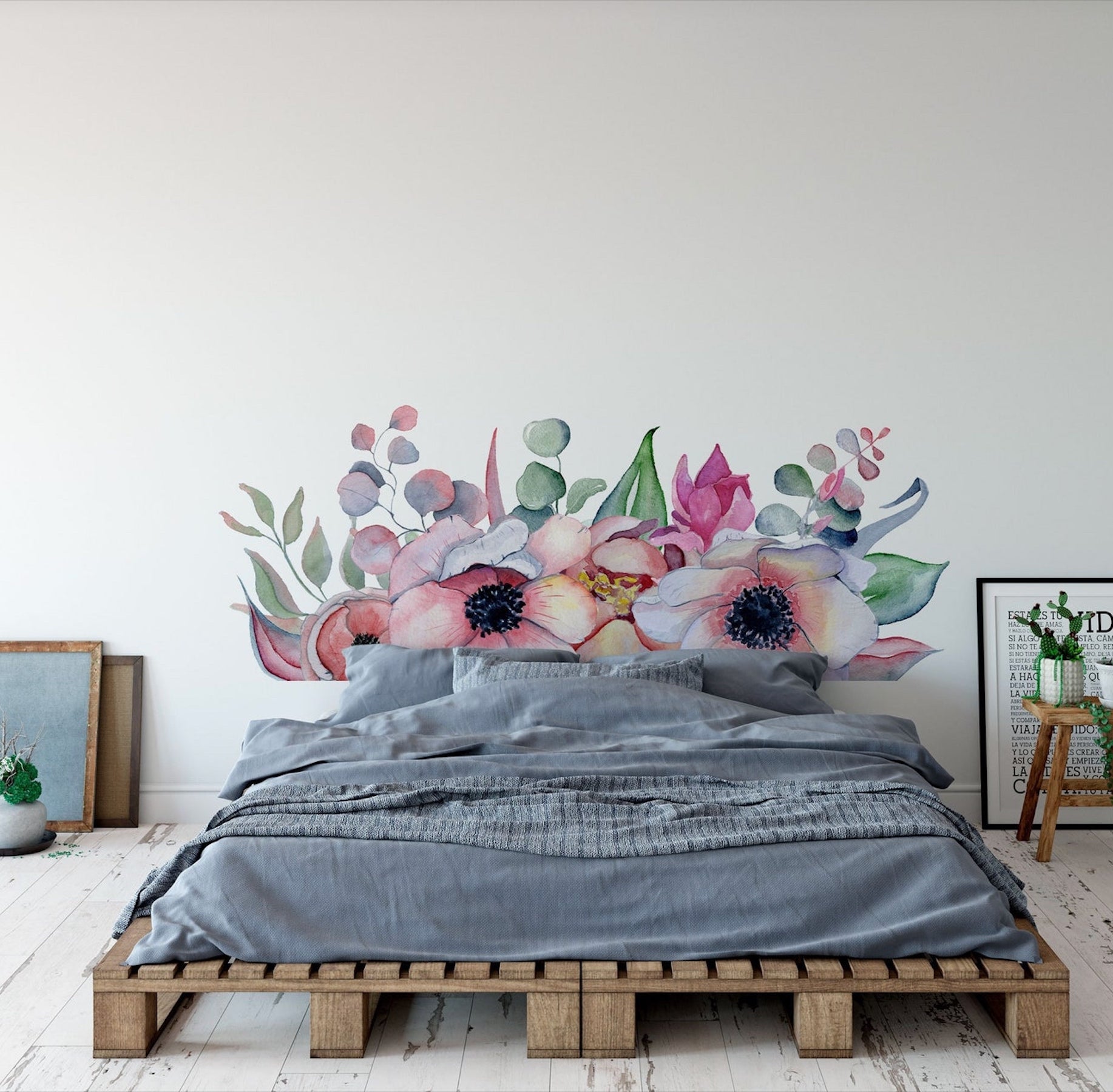 A decale with giant pansies serves as a headboard for a bed that looks as if it is sitting on palettes. The bed has gray bedding. A stool serves as an end table.