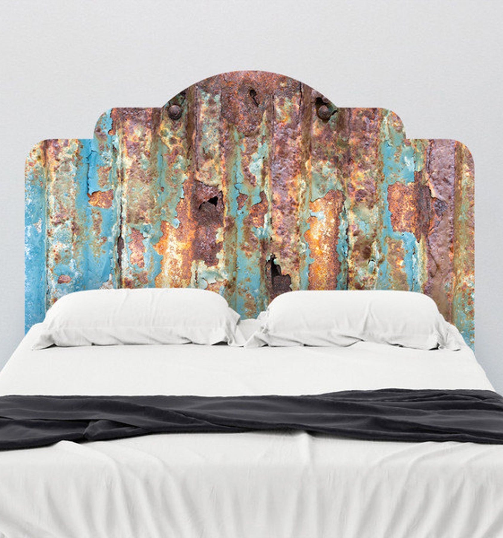 A tiered-edge decal that looks like orange, blue, and brown rusted metal serves as a headboard for a bed with white bedding. A dark gray blanket lines the bottom of the bed.