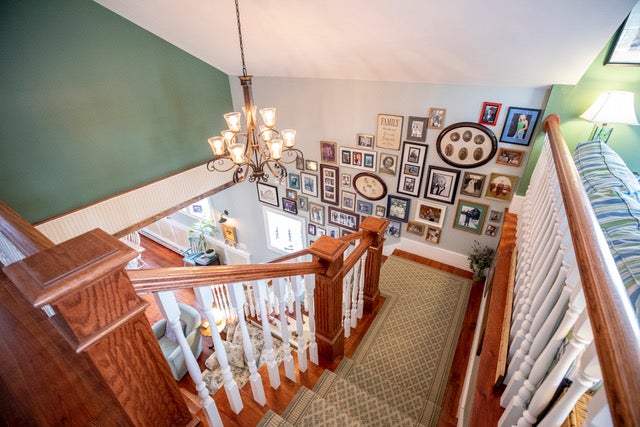 A view from a top wood stairs with white balusters and a tan patterned rug. Photos line the wall in a gallery.