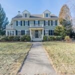 The exterior of the home is symmetrical, with several windows and two dormers. There is a large, grassy yard in front.