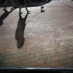 Pedestrians walking on Tremont Street cast long shadows on the brick sidewalk.