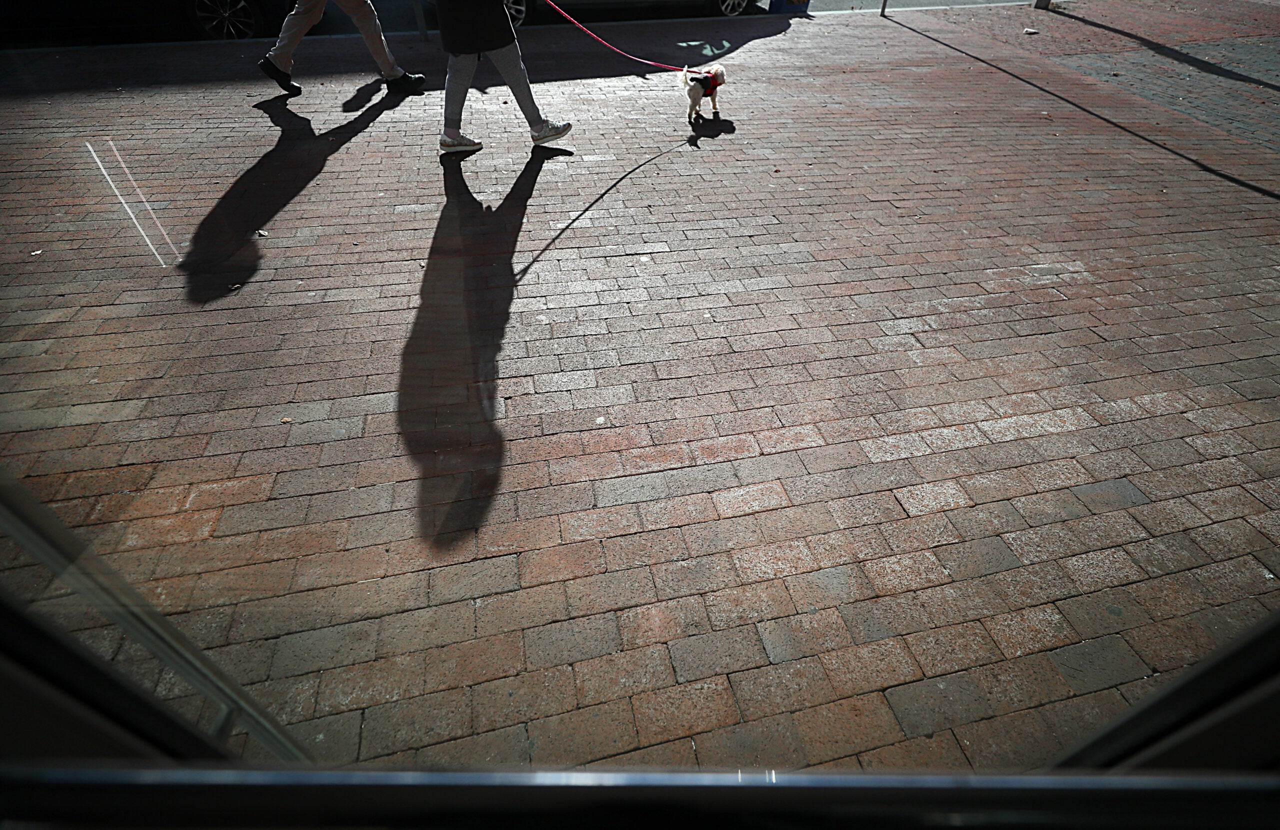 Pedestrians walking on Tremont Street cast long shadows on the brick sidewalk.
