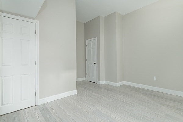 This room has gray, wood-look floors and off-white walls. There is a door in the far left corner and one in the back of the room.