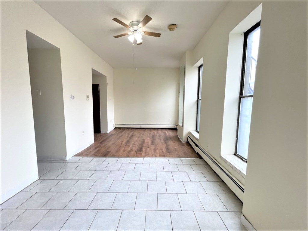 The front of the floors in this room are tile and the back half is wood. There's a ceiling fan light in the center of room, and there are three windows in the right wall letting natural light into the room.