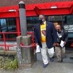 Two men in suit jackets and khaki pants exit the Urban League of Eastern Massachusetts building. Both men are wearing masks.