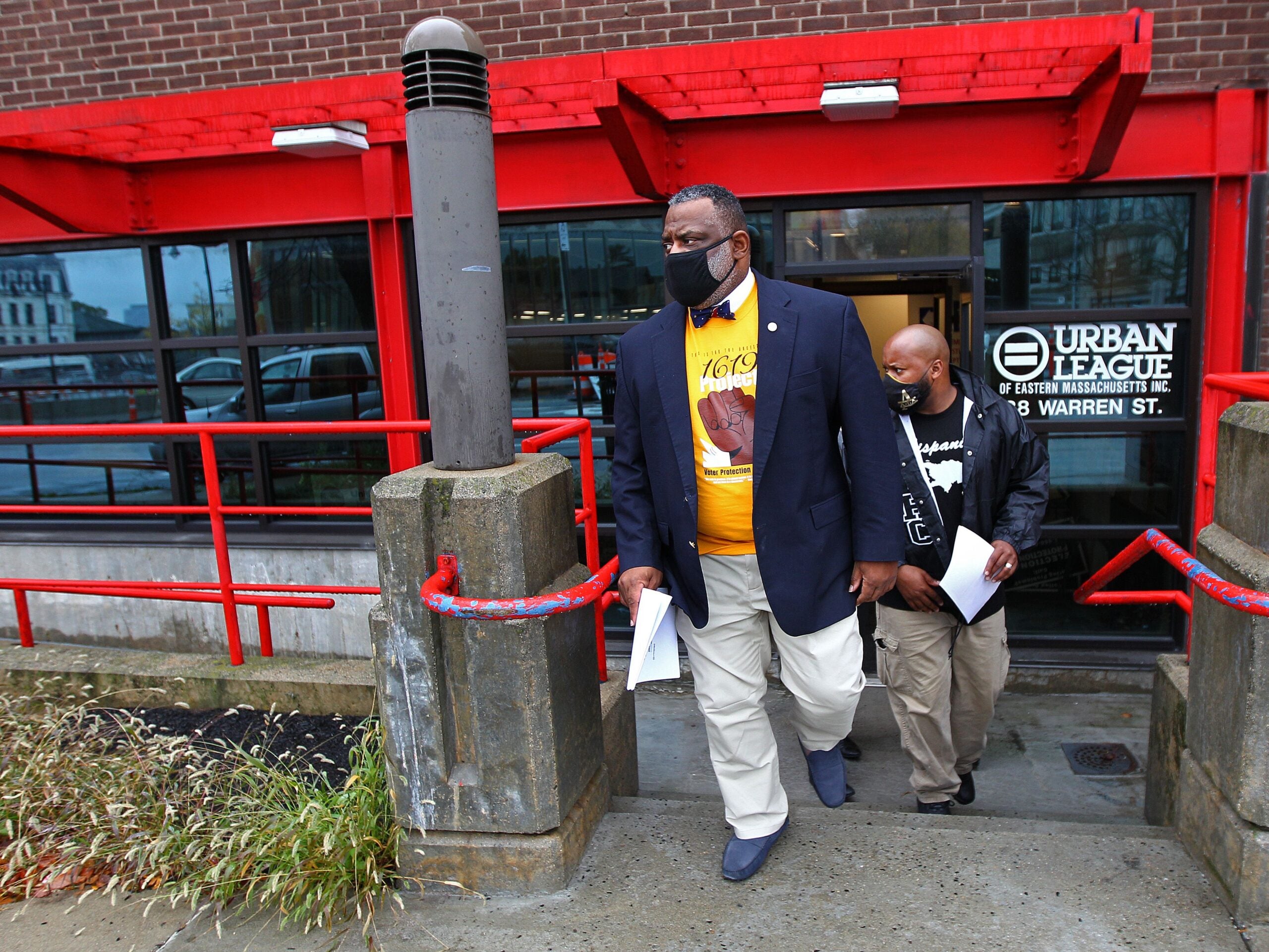 Two men in suit jackets and khaki pants exit the Urban League of Eastern Massachusetts building. Both men are wearing masks.