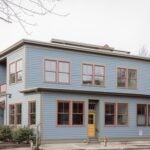 The exterior of the home is blue, with red trim around the windows. The door is yellow. The home is rectangular and has a flat roof. The sky outside is gray.