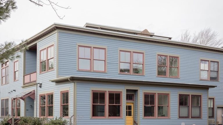 The exterior of the home is blue, with red trim around the windows. The door is yellow. The home is rectangular and has a flat roof. The sky outside is gray.