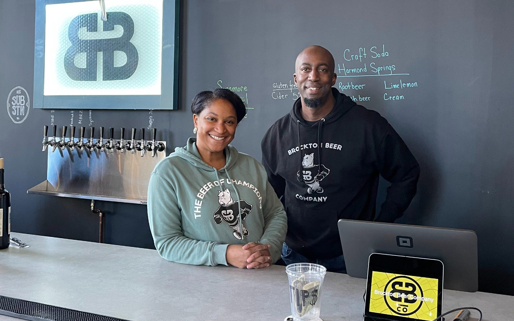 Brockton Beer cofounders and married couple LaTisha and Eval Silvera pose behind the bar at the Roslindale Substation
