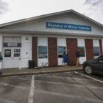 The Brockton Registry of Motor Vehicles as seen from the outside: A single-story white and red-brick building with a blue sign reading "Registry of Motor Vehicles."