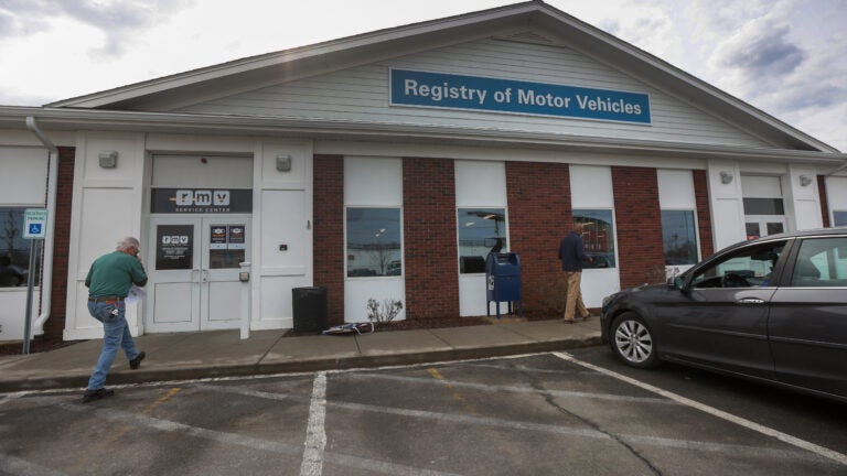 The Brockton Registry of Motor Vehicles as seen from the outside: A single-story white and red-brick building with a blue sign reading "Registry of Motor Vehicles."