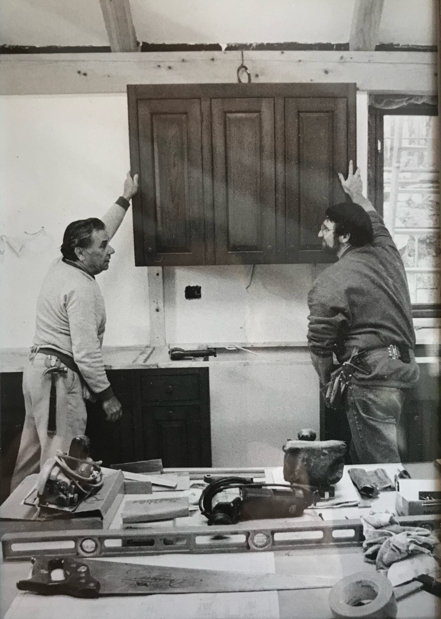 Norm Abram and his father install cabinets in a black-and-white photo.