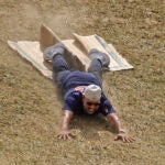 Alex Cora smiles as he slides head-first down a hill on a piece of cardboard.