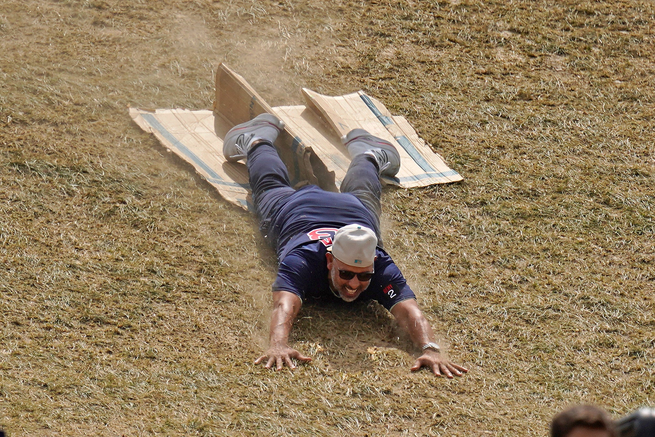 Alex Cora smiles as he slides head-first down a hill on a piece of cardboard.