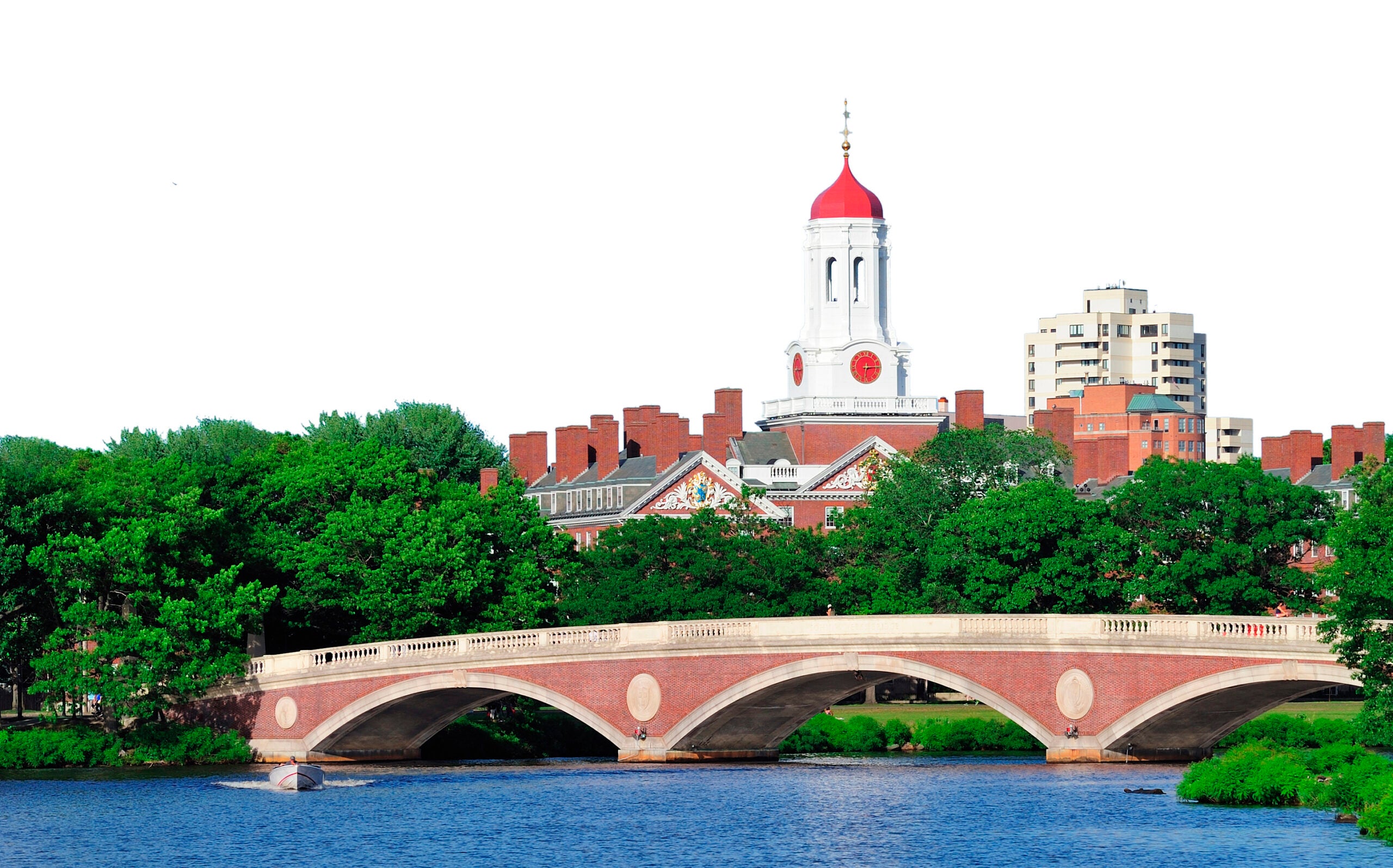 John W. Weeks Bridge and clock tower over Charles River in Harvard University campus in Boston with trees and blue sky.