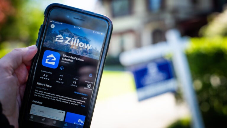 picture of cellphone with zillow ap in front of home for sale