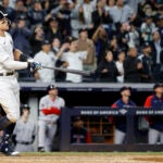 Aaron Judge, Yankees fans, and the Red Sox dugout watch Judge's high fly ball soar toward the fence.