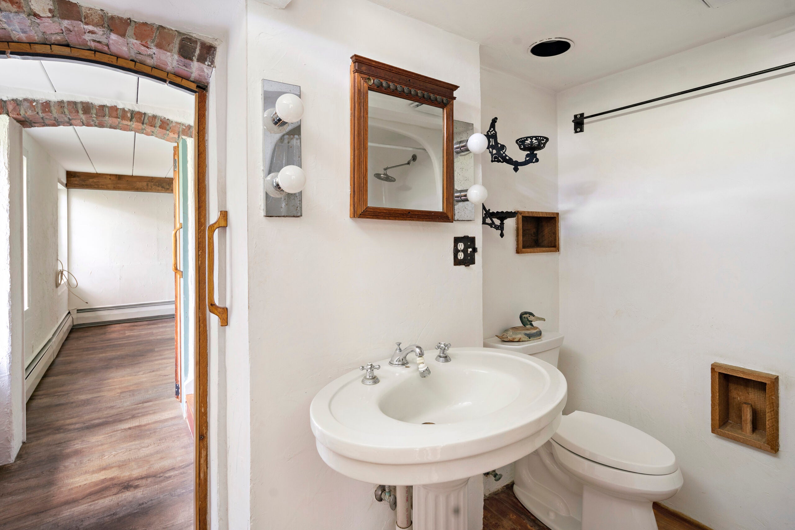 A bathroom with a brick archway and a pedestal sink.