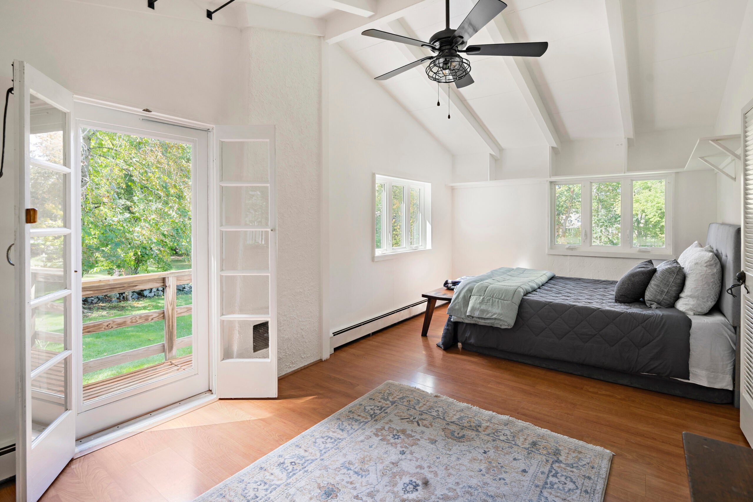 A bedroom with a ceiling fan, exposed beams, and French doors to a deck.