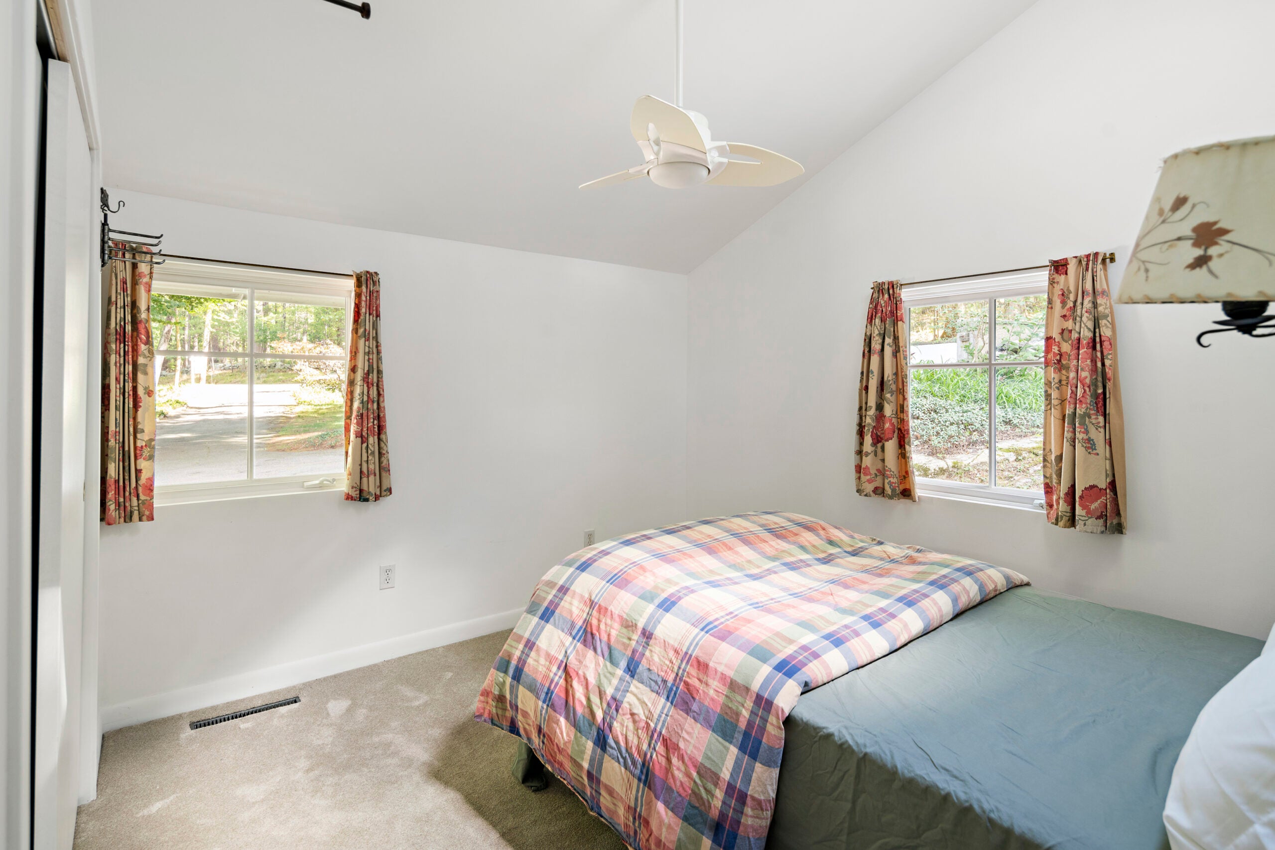 A carpeted bedroom with a small ceiling fan and two-over-two windows.