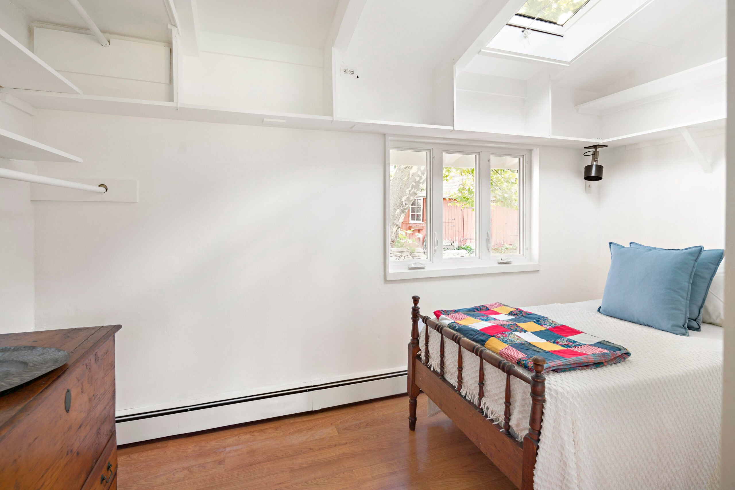 A small bedroom with white walls, a skylight, and cubbies at ceiling level.