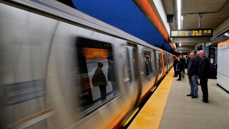 A newer model Orange Line train is a blur as it speeds by riders waiting on the platform.