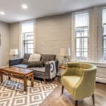 A living room with modern gray and green furniture, several tall and narrow windows, and gray walls.
