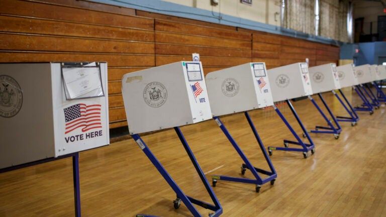 alt = white voting booths with American flags on them in a wood-paneled gymnasium