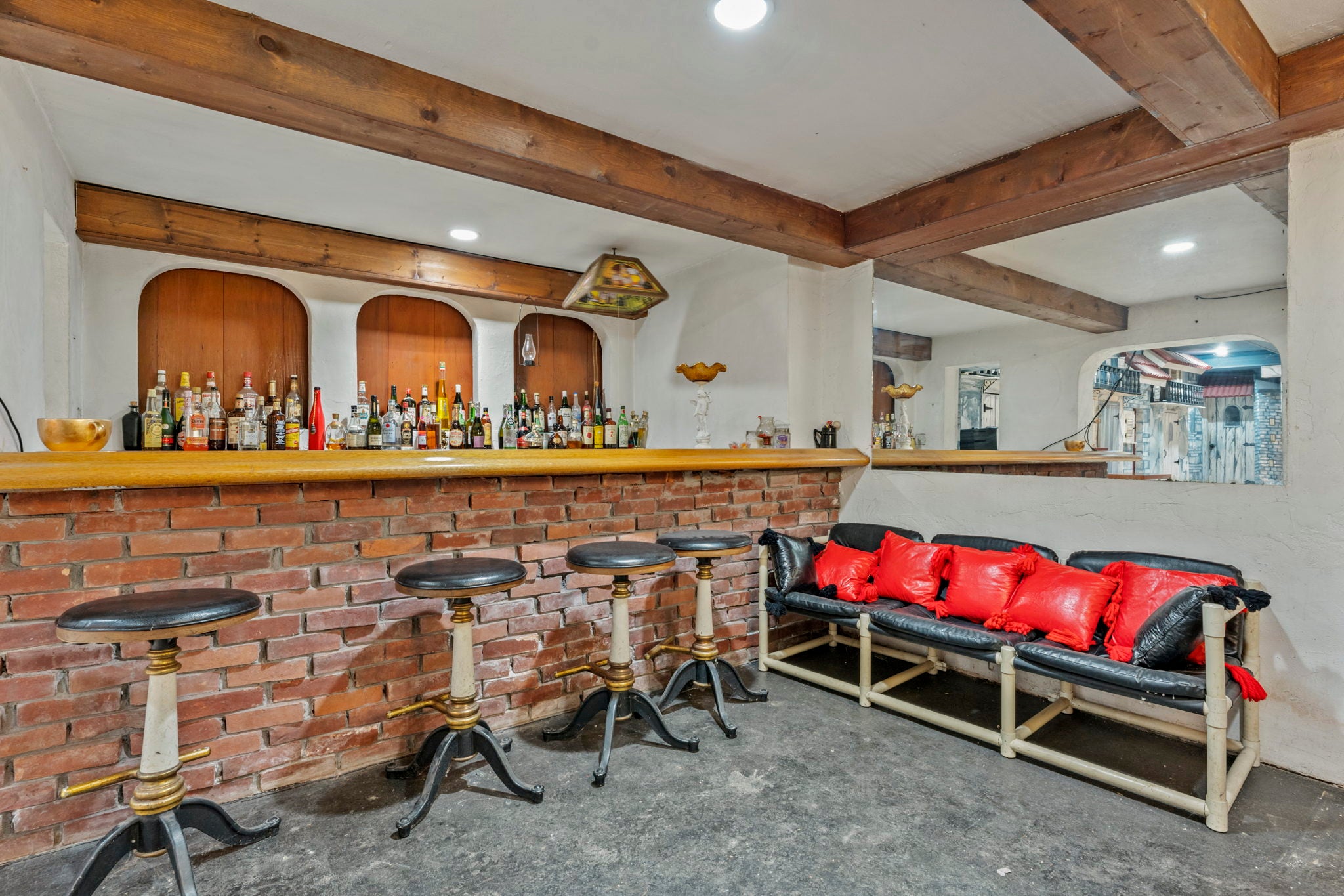 A wide brick bar with seating for four. Dozens of bottles of liquor line the back wall, which features exposed beams and cutouts with wood backgrounds.