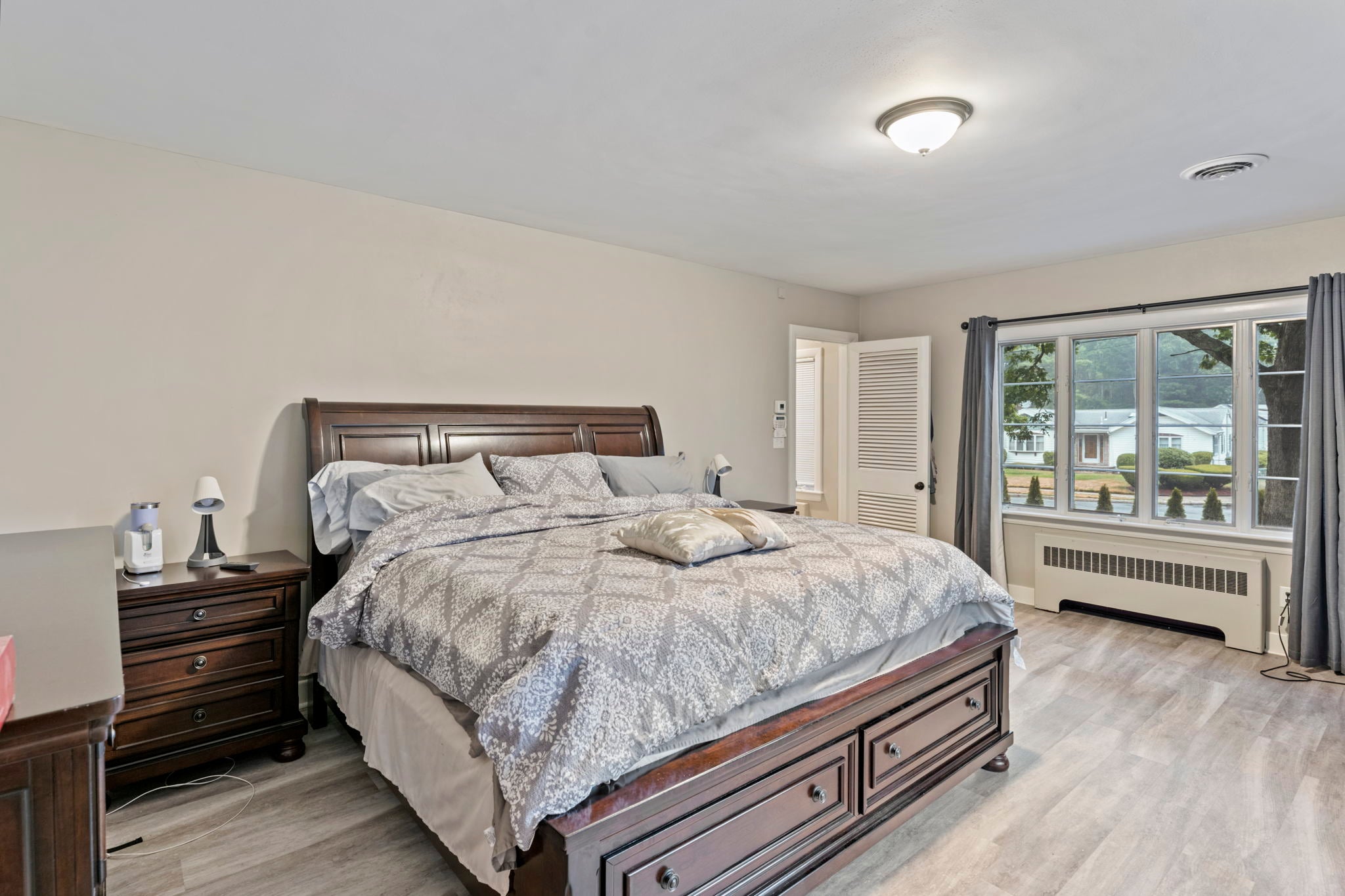 A bedroom with neutral colored walls, flooring that lookslike wood, and a grouping of four windows.