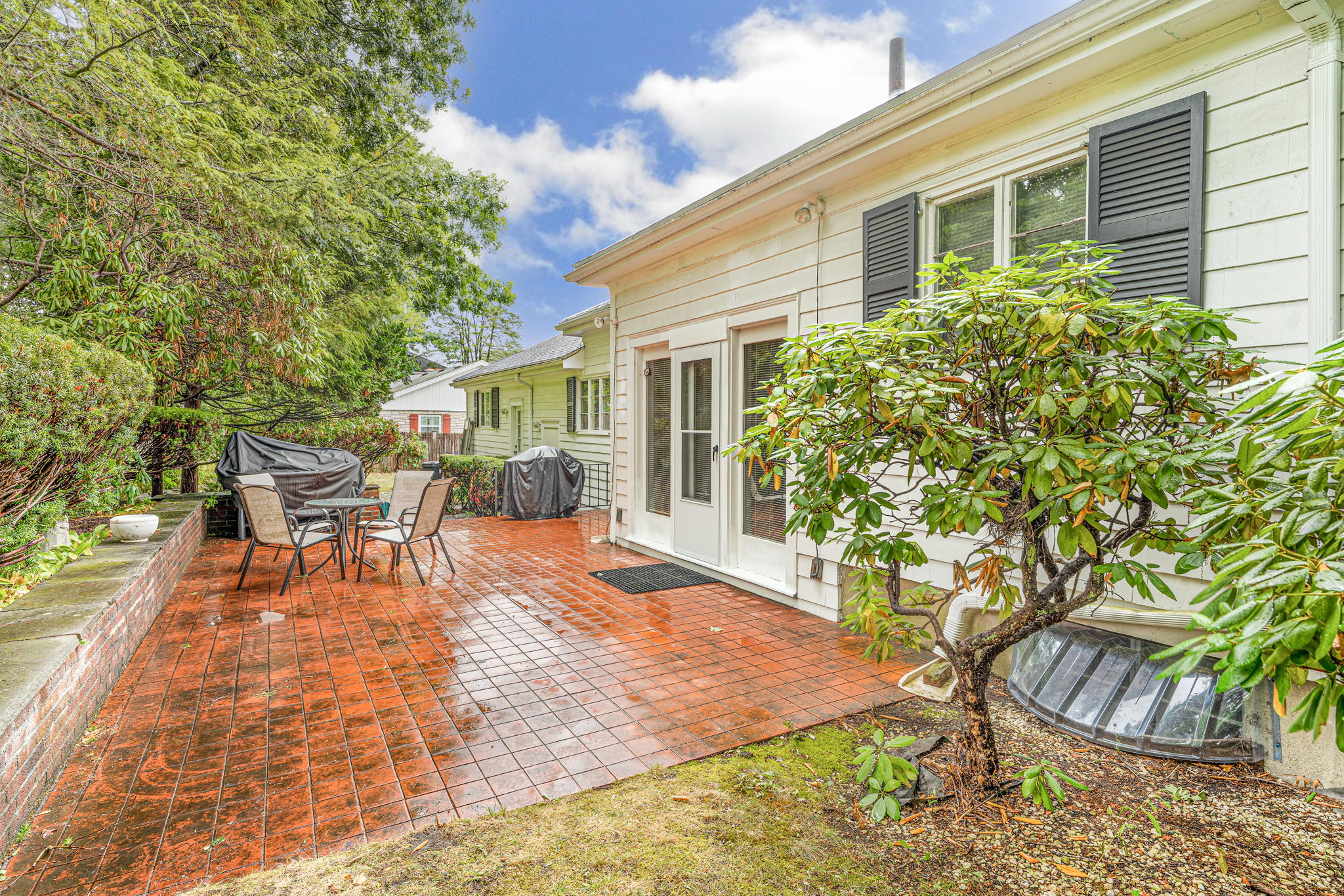 A brick patio next to a one-story white house with dark shutters.