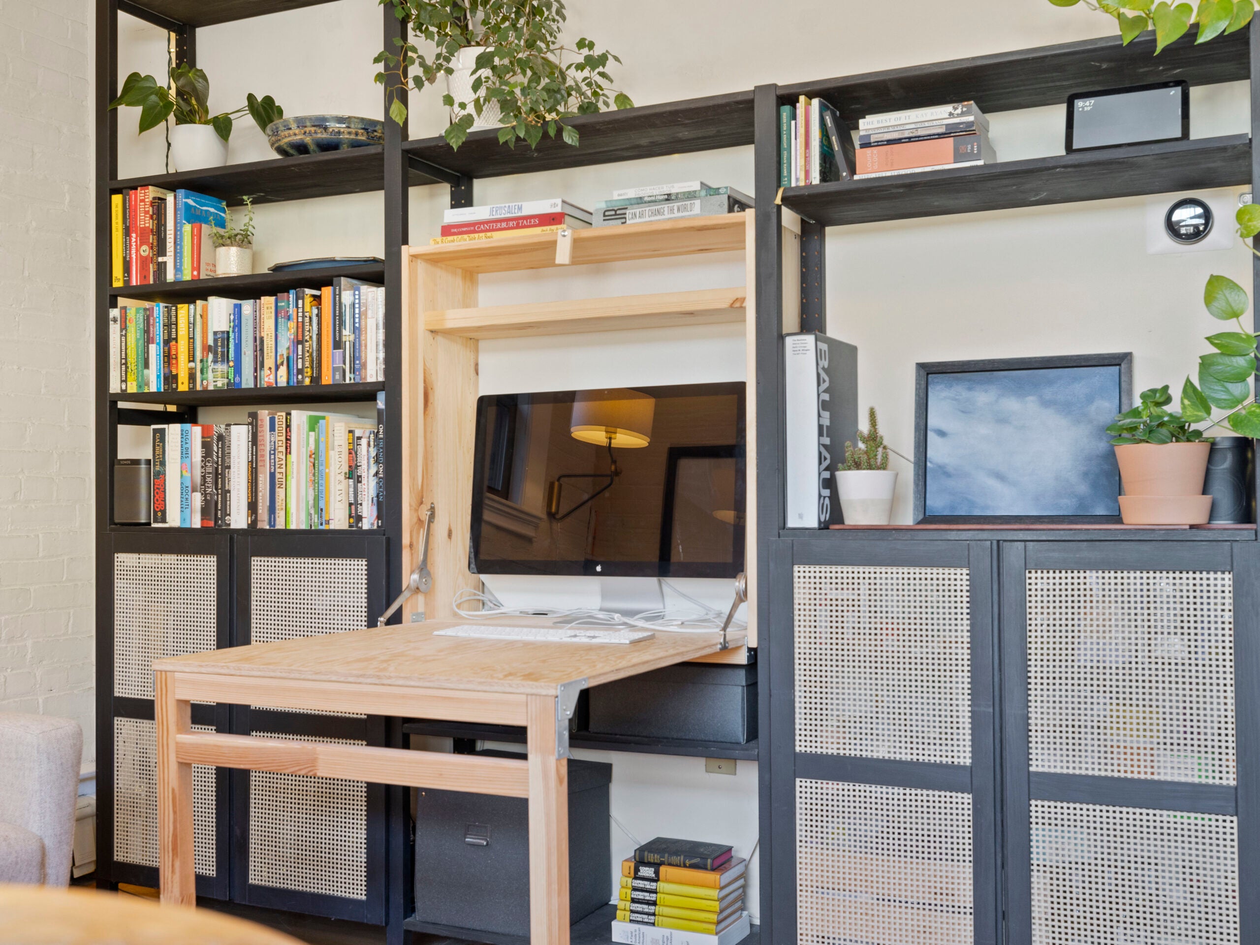 A built-in desk offers a way to open up the space. The shelving surrounding it is black. Some have rattan doors.