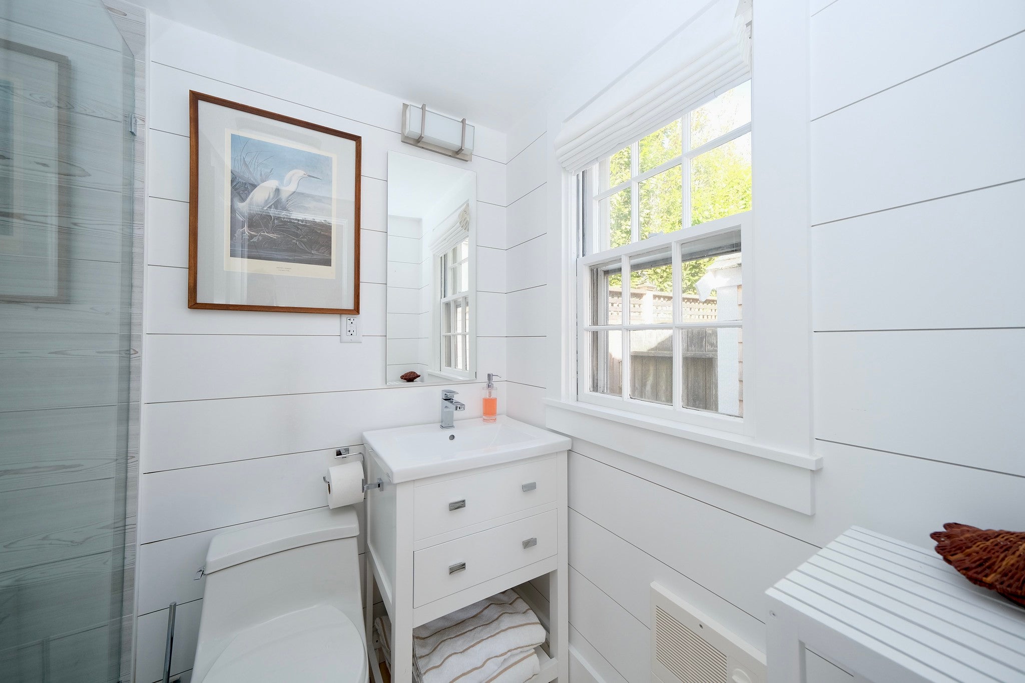 White shiplap walls a small sink with white cabinetry, and a standalone shower.